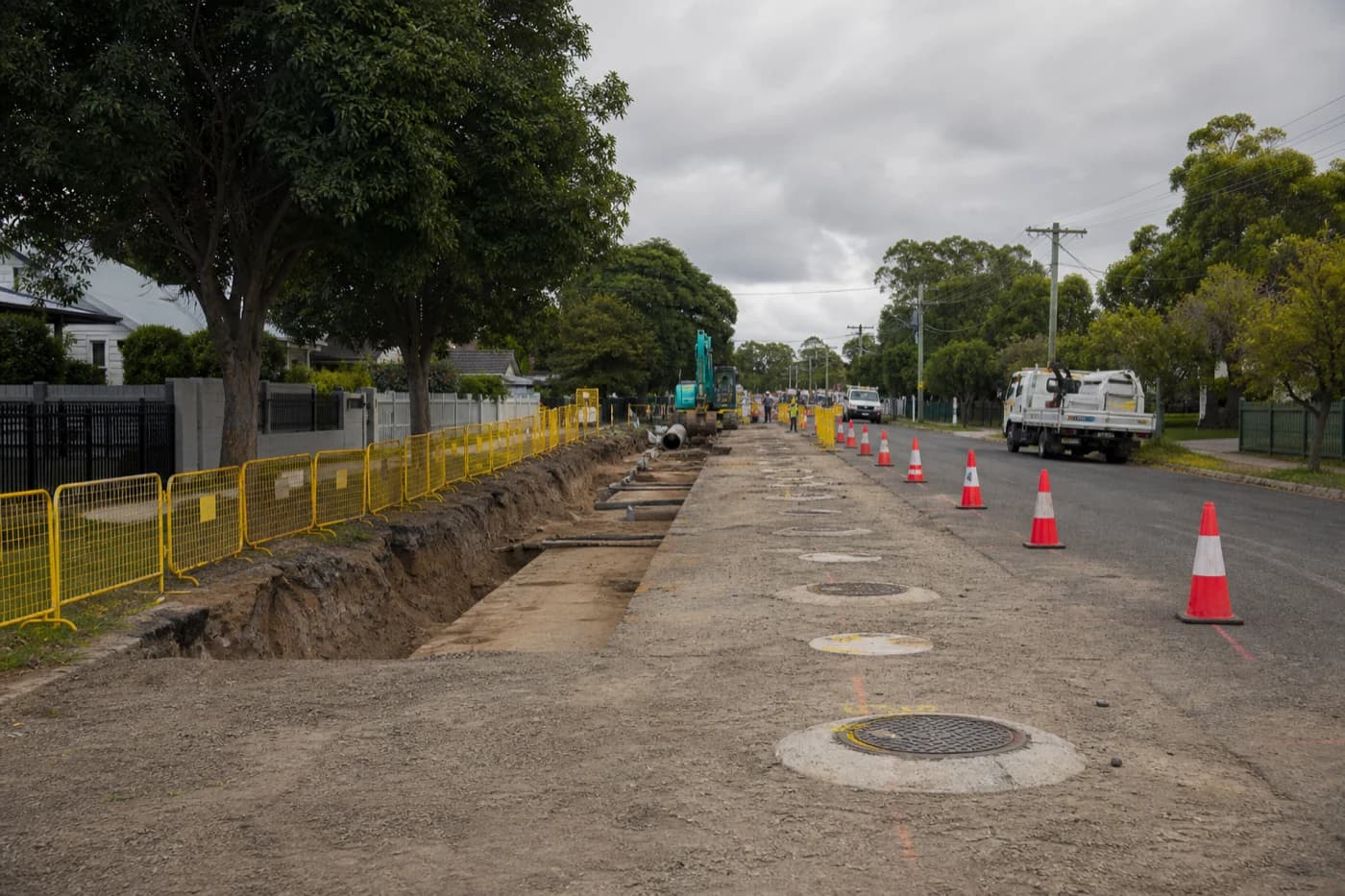 NSW residential street with staged sewer renewal corridor, manhole works, and traffic management along a suburban frontage